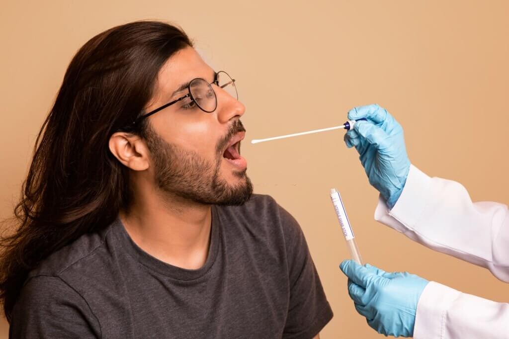 Nurse taking oral swab for saliva sample test from a long-haired indian man