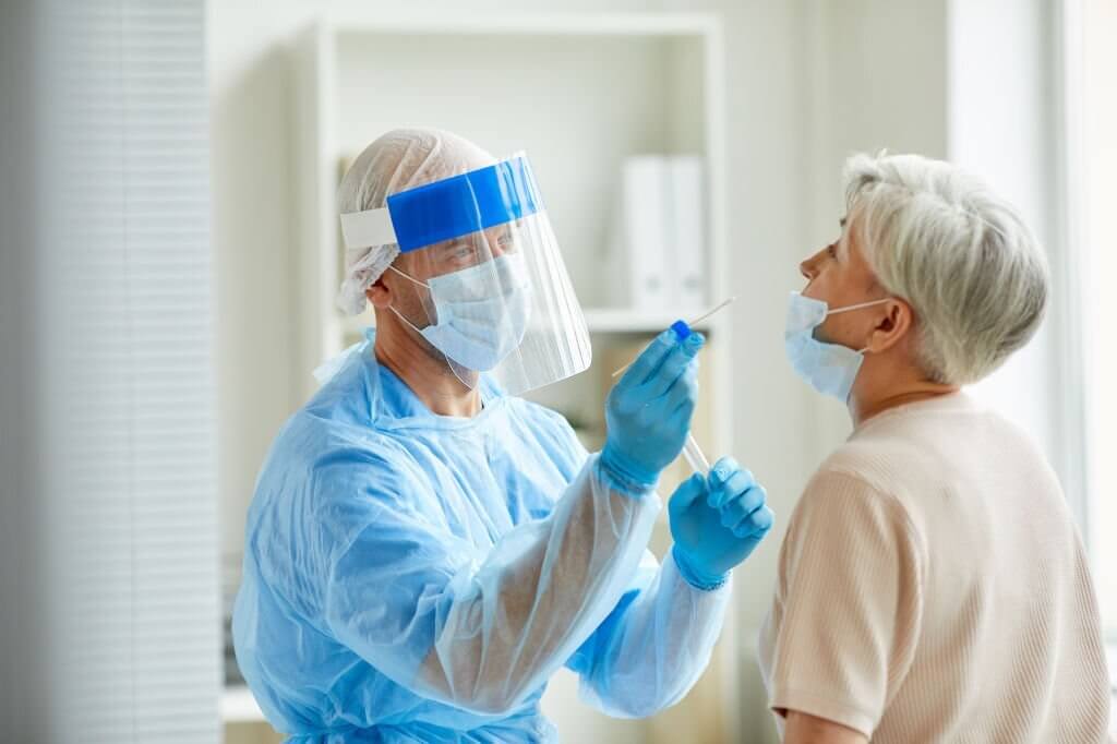 Modern laboratory worker wearing personal protective equipment testing senior woman for coronavirus using nasal swab method