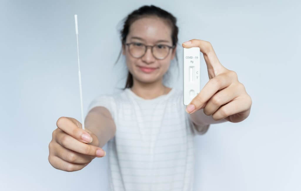 Asian woman holding a disposable sterile flocked swab with a test pad