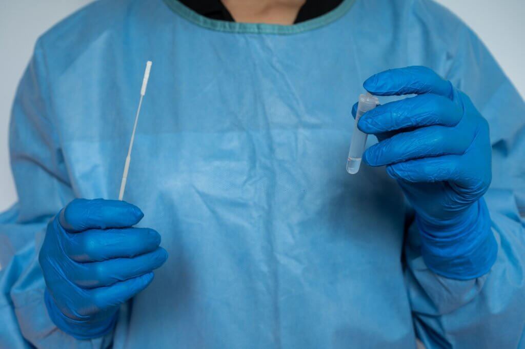 Healthcare worker holding a disposable sterile flocked swab with a collect tube