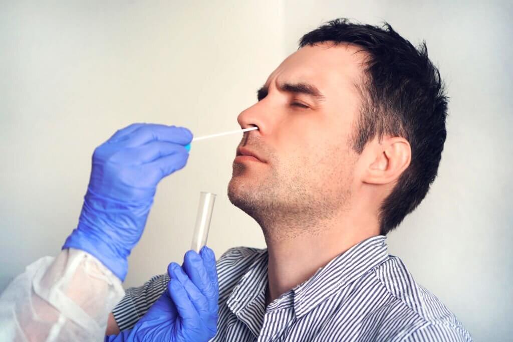 A doctor in a protective suit taking a nasopharyngeal swab from a man