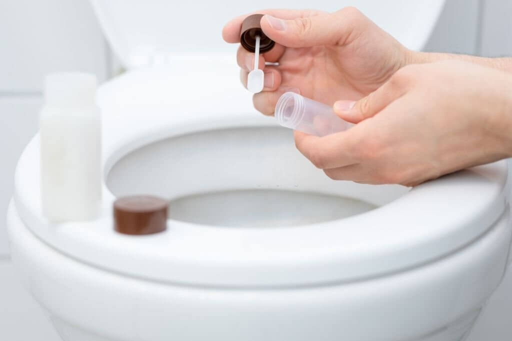 The male hands on toilet with plastic bottle in hand collecting stool sample of his fecal with shovel