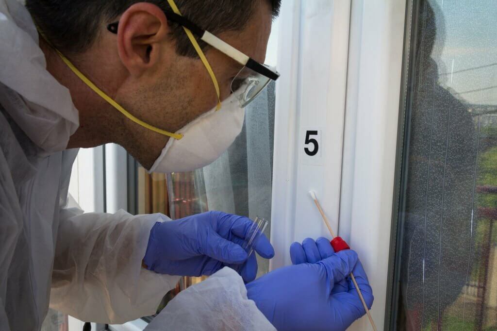 Forensic expert takes a sample of the DNA analysis on sterile swab from the window