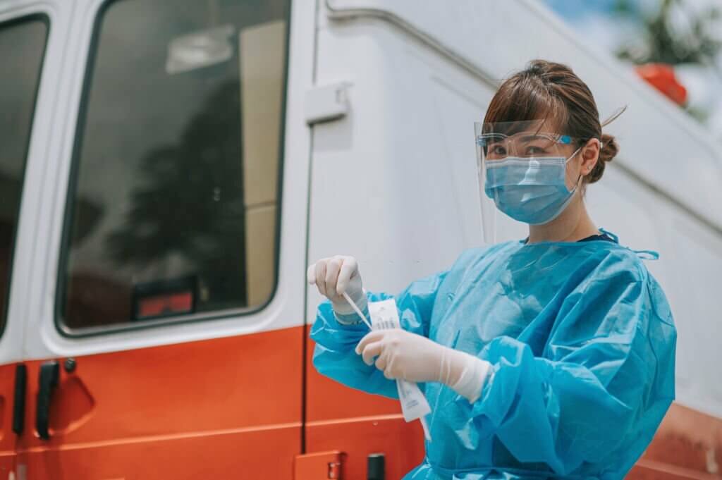 Outdoor beside ambulance Asian chinese female doctor with PPE getting ready taking nasopharyngeal swabs from patients